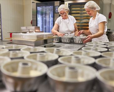 Junge Frau als Bäcker Lehrling beim Gugelhupf backen unter Anleitung in der großen Bäckerei